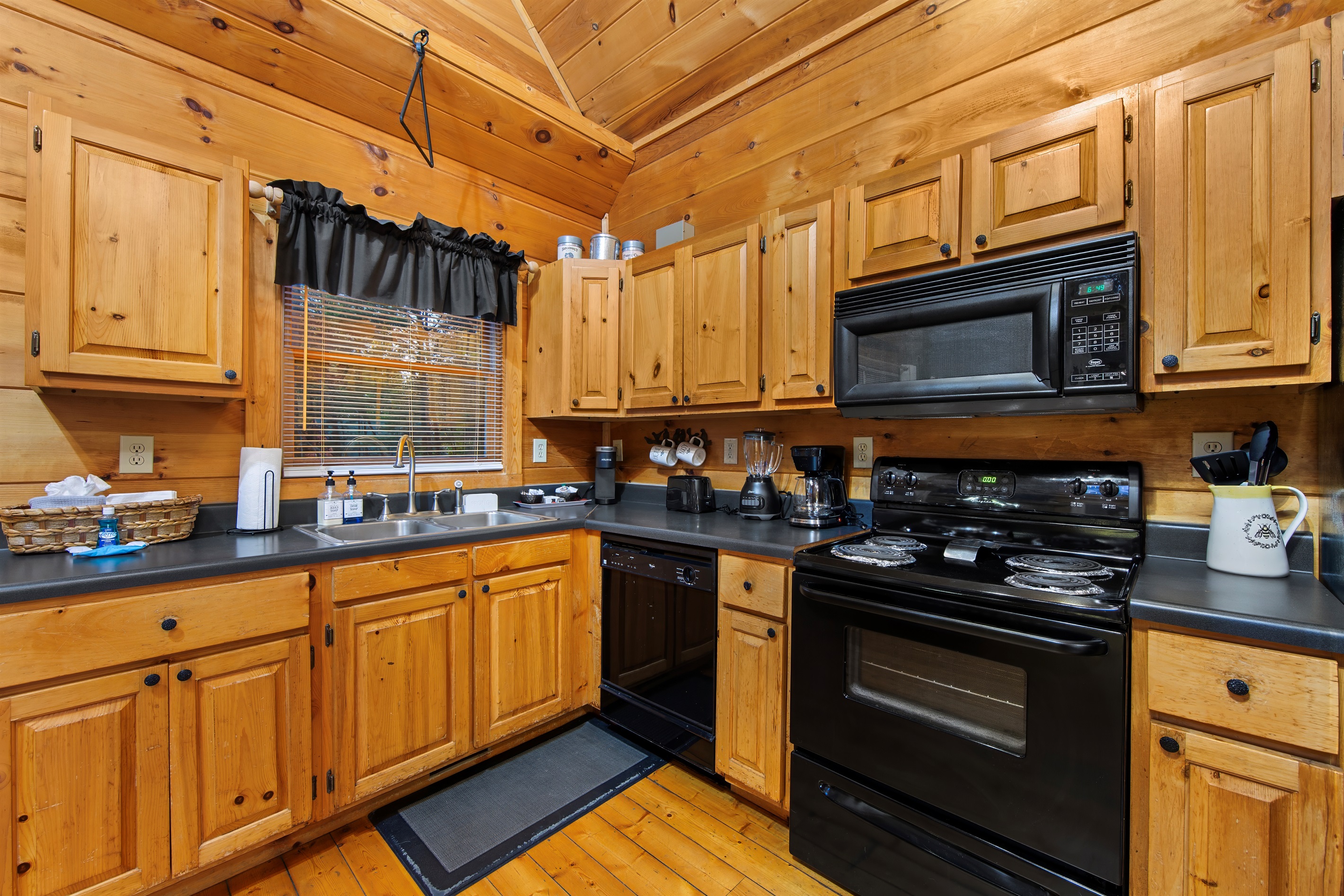 A fully equipped rustic kitchen features black appliances, a double sink, and warm wood cabinetry, maintaining the cabin's cohesive aesthetic.