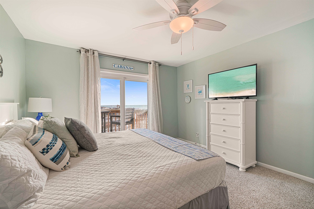 Wall-mounted flat-screen TV and a sliding door to the dune-front deck. The king master at The Gathering Place is hard to leave.