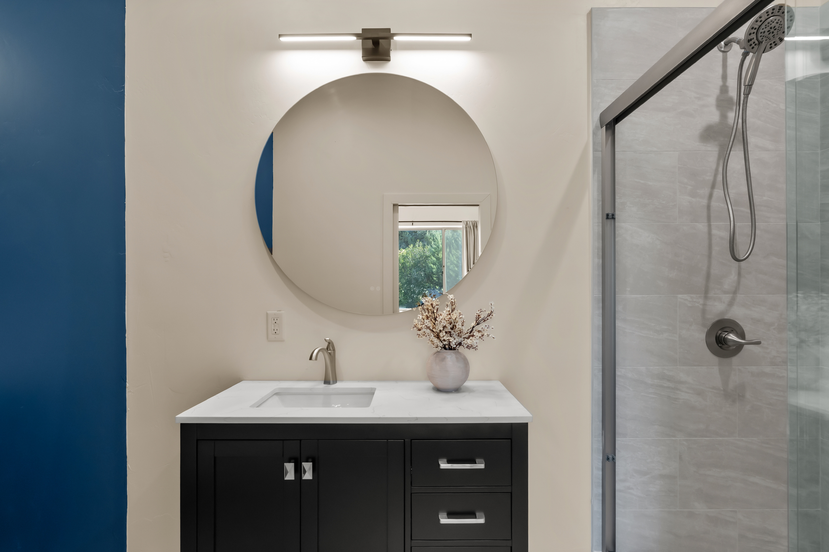 Clean contemporary vanity area complete with quartz countertops, modern brushed fixtures, a chic round mirror, and warm designer vanity lighting.