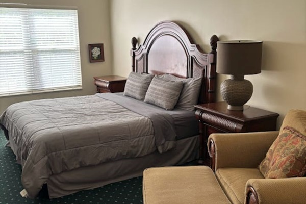 Inviting bedroom featuring a large bed, seating area, nightstand, and bright window view.