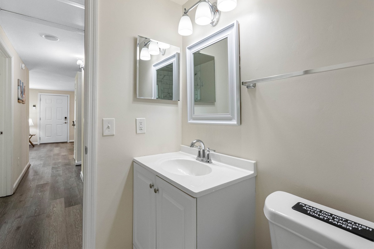 The space features a classic white vanity with chrome fixtures, topped with a smooth integrated sink and matching framed mirror above.