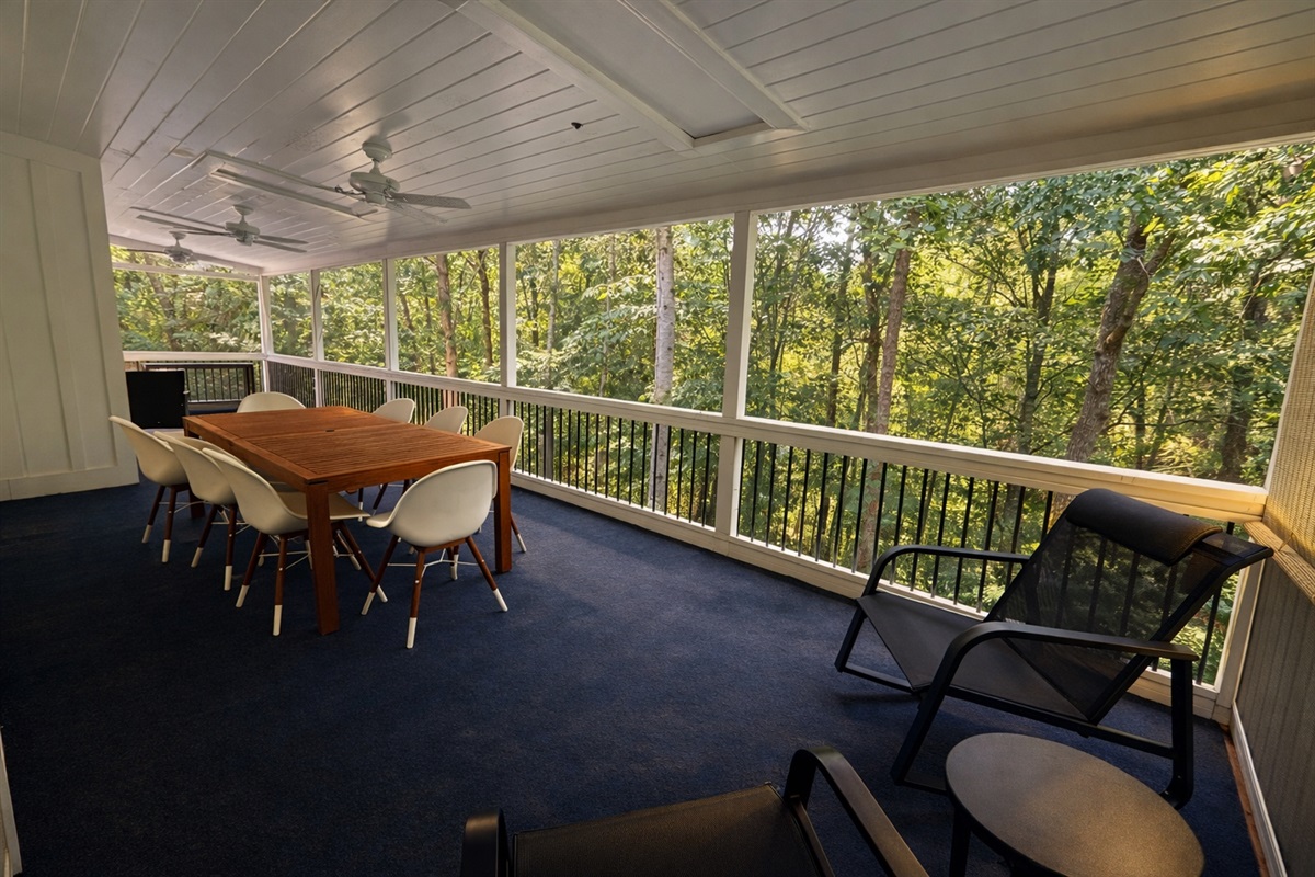 Spacious screened-in porch with dining area and comfortable seating overlooking the peaceful wooded surroundings.