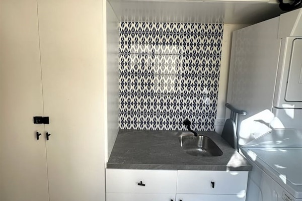 Discover our custom-built laundry and sink, designed to meet all your clothes care needs, complete with a clothes drying rack, ladder, mops, and brooms conveniently stored behind the door.