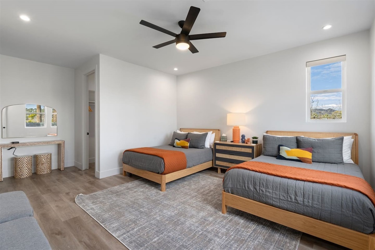 Enjoy relaxation in this spacious bedroom with two double beds, a bedside table, a ceiling fan, and a TV, complemented by a stylish vanity area and a private bathroom for a pleasant stay.