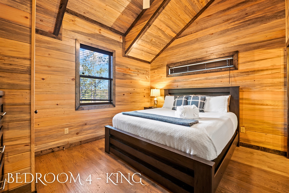 Showcasing a minimalist aesthetic, this bedroom features a dark wood bed with white bedding, complemented by the warmth of wood walls and a vaulted ceiling.