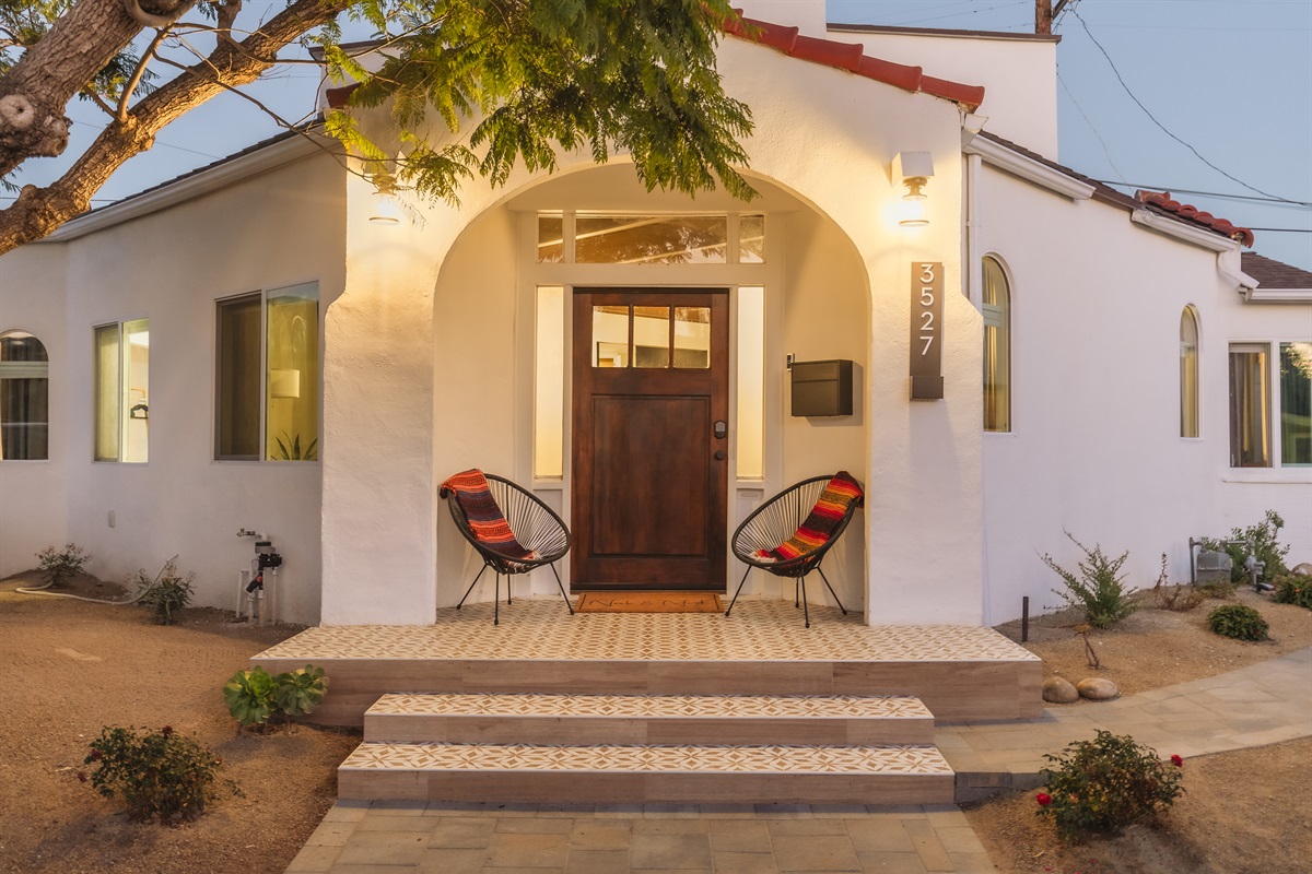 Charming Entrance: Relax on chairs by the stylish doorway of this Spanish style home under San Diego's warm sun!