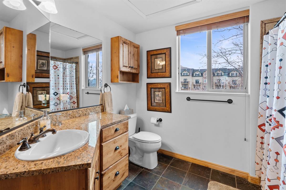 Bright primary ensuite bathroom featuring a granite vanity, natural light, and mountain charm.