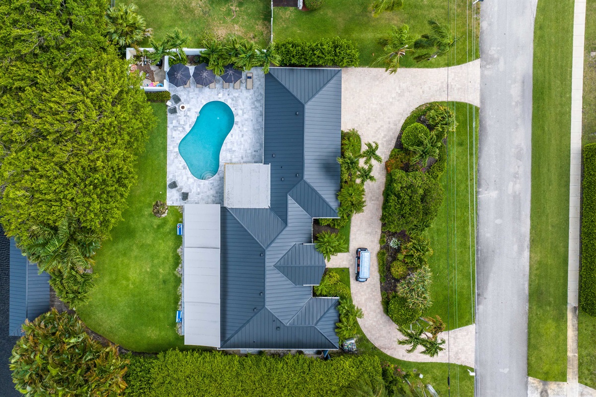 This aerial view highlights the full Oasis Palms layout, with the pool, lawn, driveway, and waterfront setting all in one clear view.
