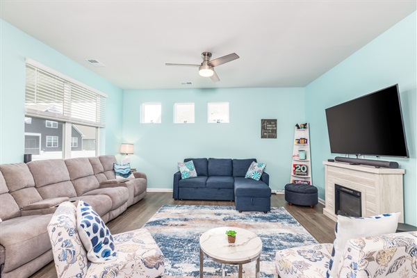 Family lounge featuring a plush recliner sofa, blue sleeper-sofa, and smart TV above a decorative fireplace—ideal for movie nights, board games (shelf stocked with puzzles) or cozy relaxation.