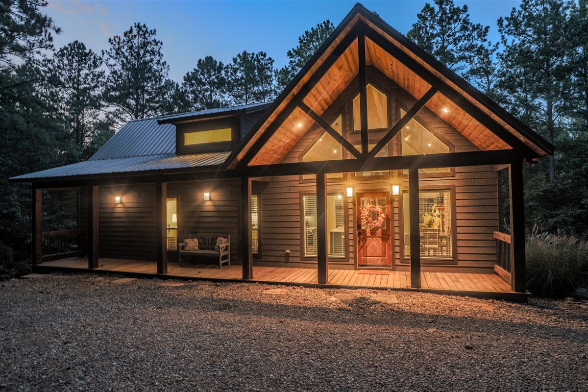 Exterior Retreat: Charming cabin with warm lights, inviting porch, and nature at your doorstep!