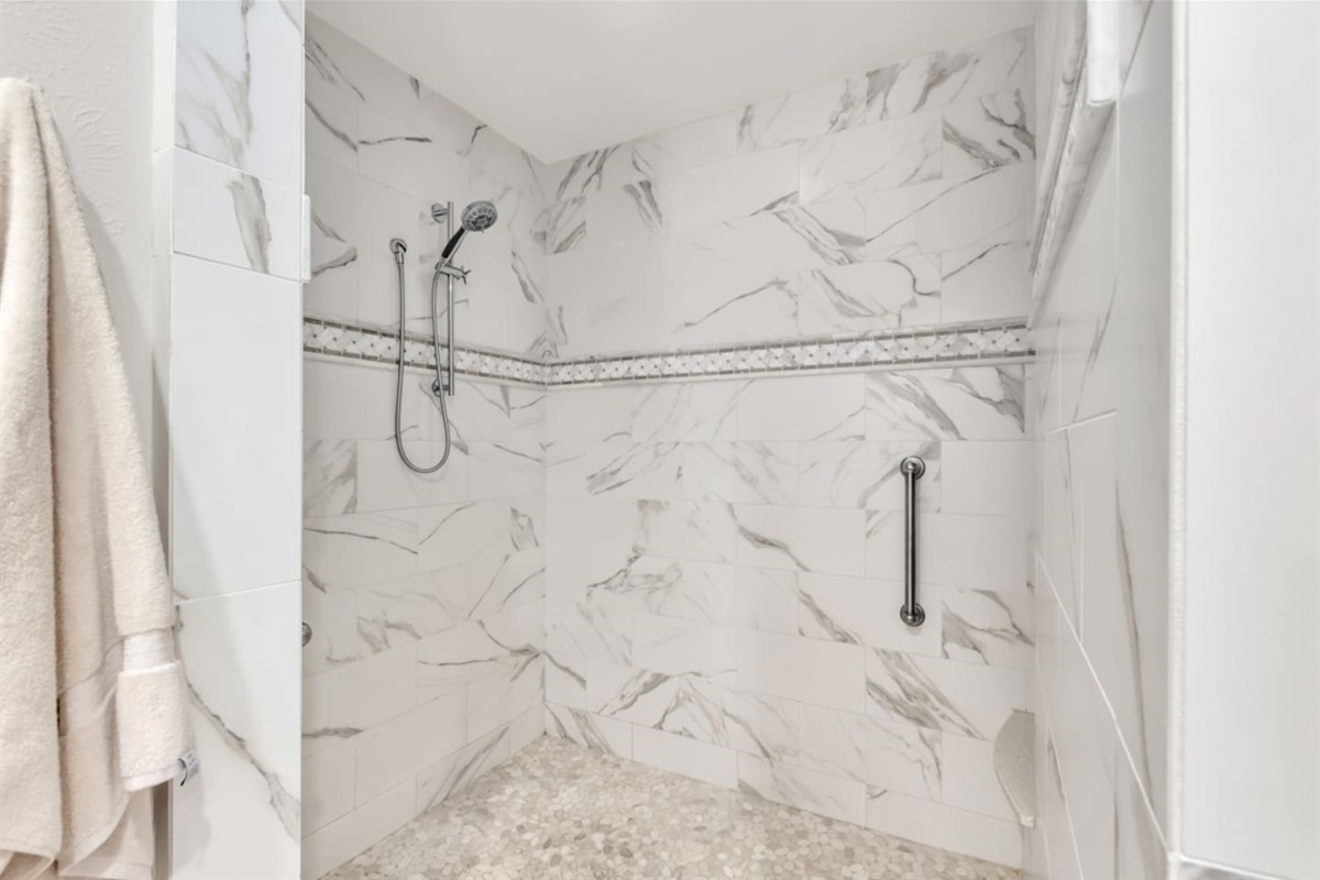 Step-free primary shower with a handheld shower head and built-in seat, featuring ADA-grade accessibility for comfort and ease of use.