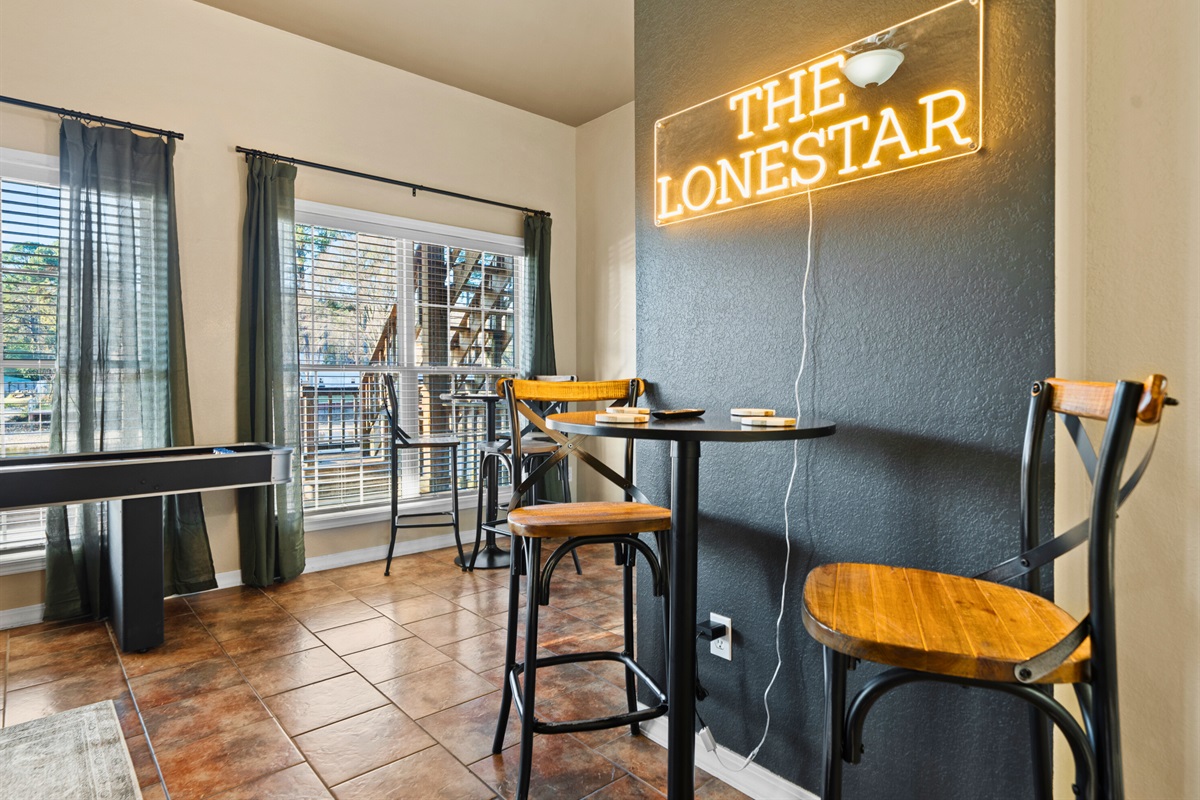 The tall bar table beneath The Lonestar sign creates a cozy spot to enjoy drinks, snacks, or a quick break between games, adding a fun lounge feel to the entire room.