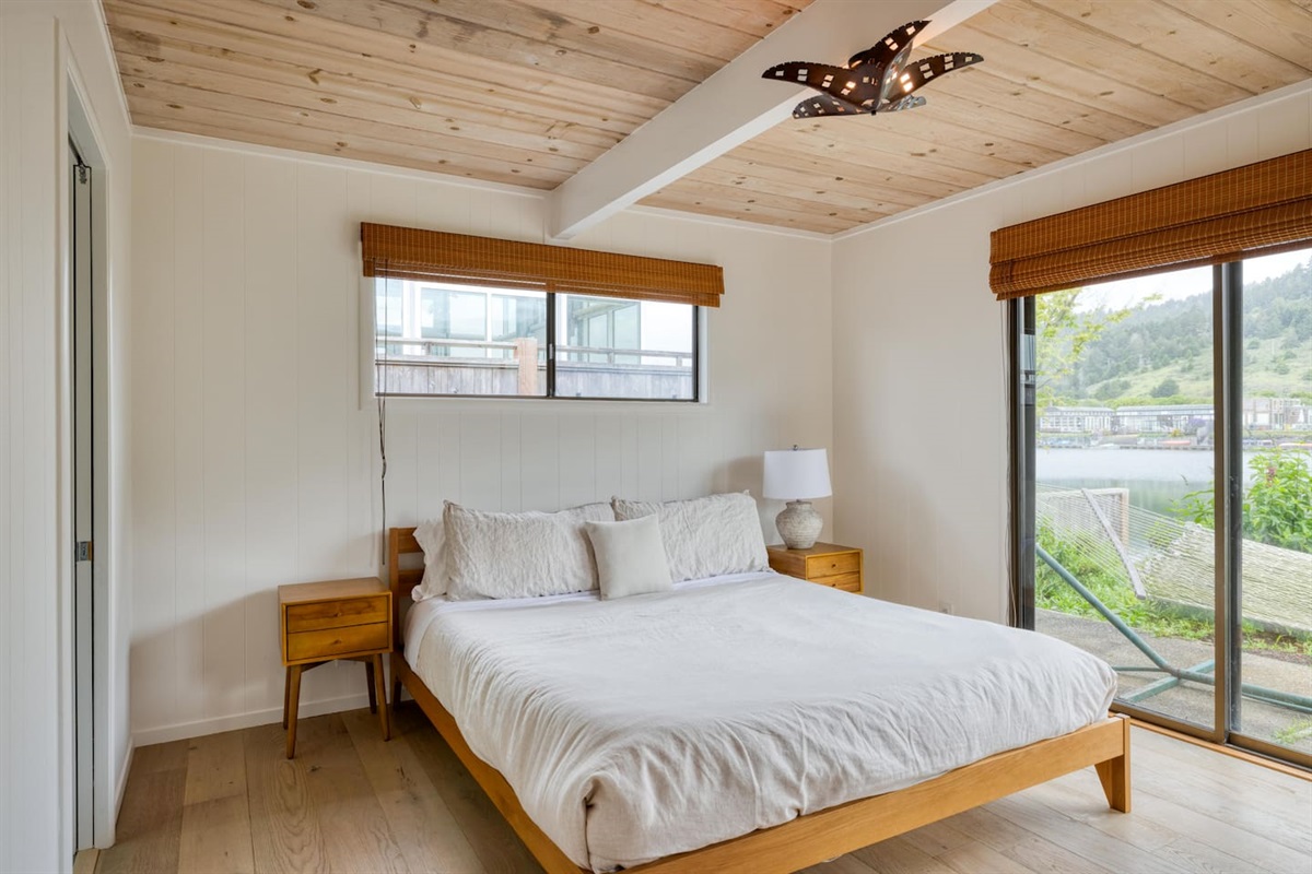 - Bright bedroom with queen bed and sliding glass doors to a waterfront patio  
- Wooden ceiling and matching furniture create a warm and inviting retreat  
- Large windows fill the room with natural light and scenic outdoor views  
