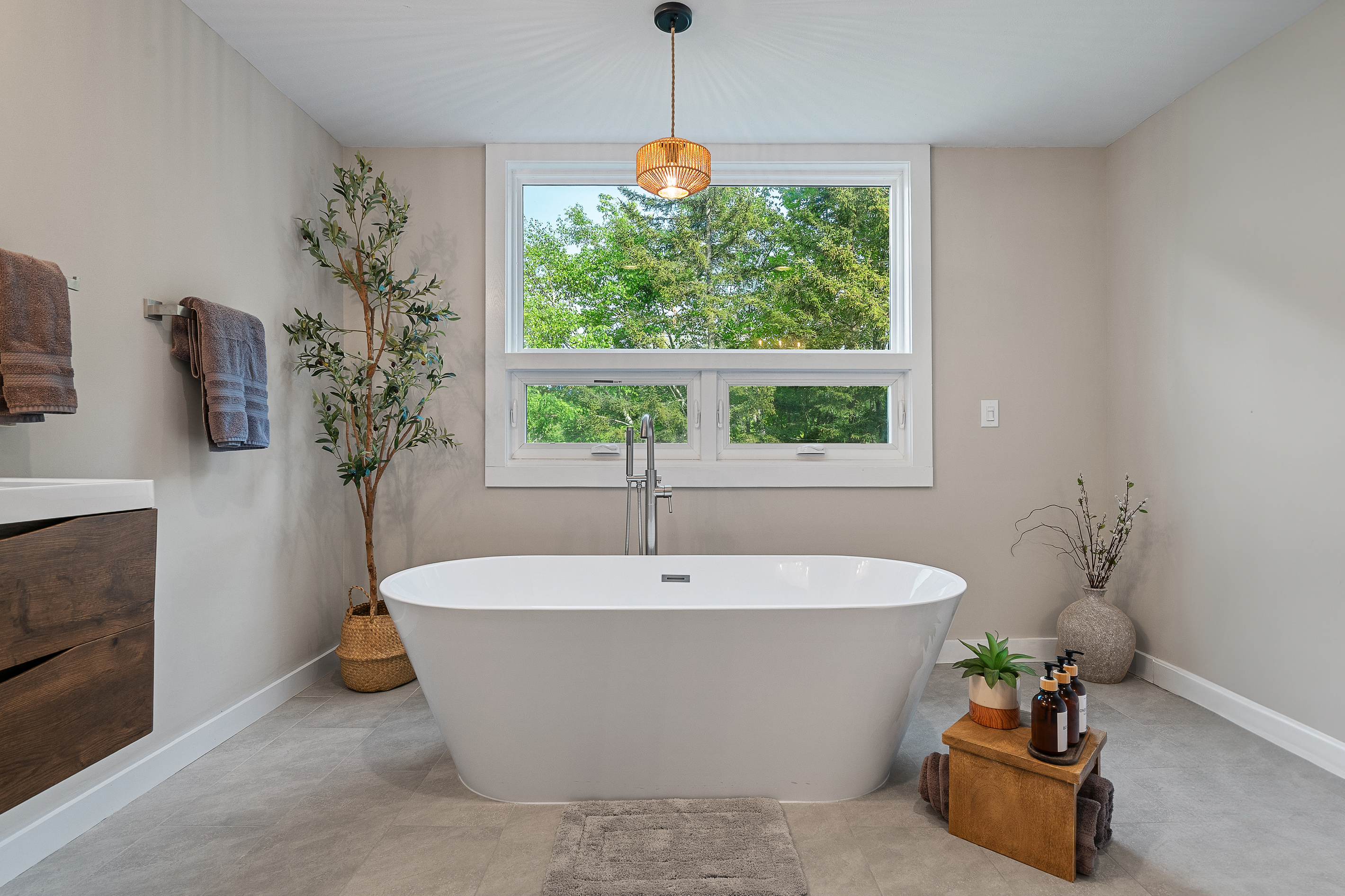 Freestanding soaking tub beside a forest-view window for post-ski recovery