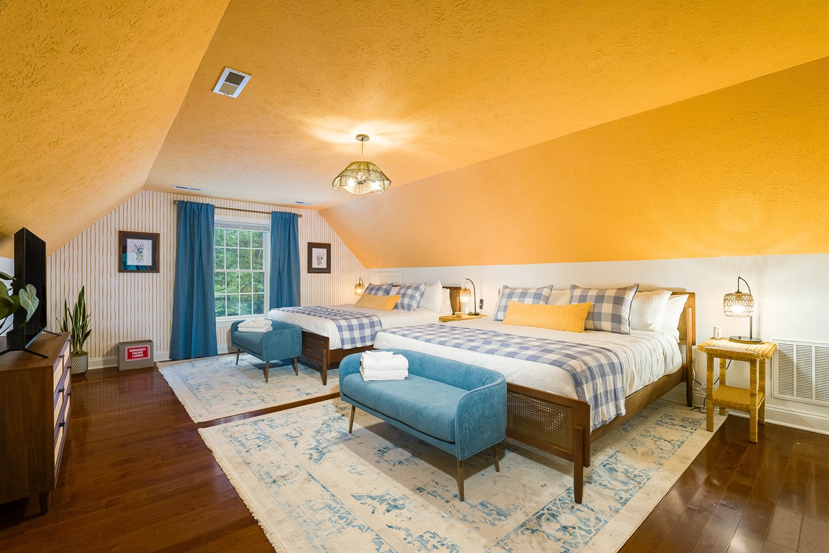 A spacious retreat designed for groups or families, featuring two king beds, matching benches, and a cheerful mix of bold ceiling color and patterned bedding. With a TV and plenty of floor space, it’s a comfortable spot for unwinding after a day of adventu