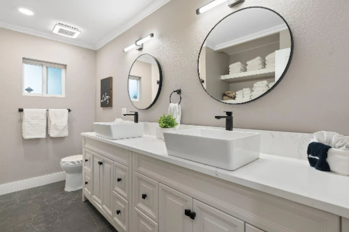 A long dual vanity with vessel sinks gives this bathroom plenty of room to spread out, while round mirrors and stacked fresh towels add a spa-like finish. Natural light from the window keeps the space feeling bright throughout the day.