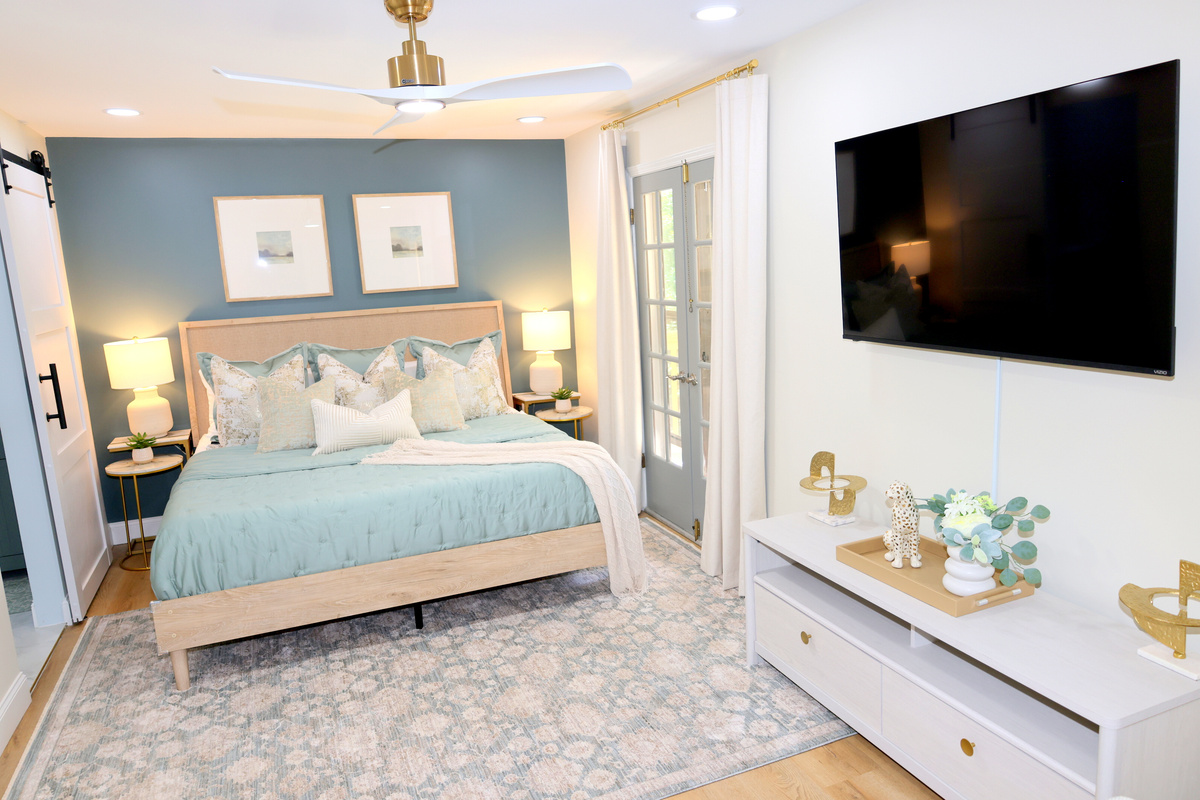 Beautiful primary bedroom with luxury bedding, accent wall, large TV, and elegant finishes