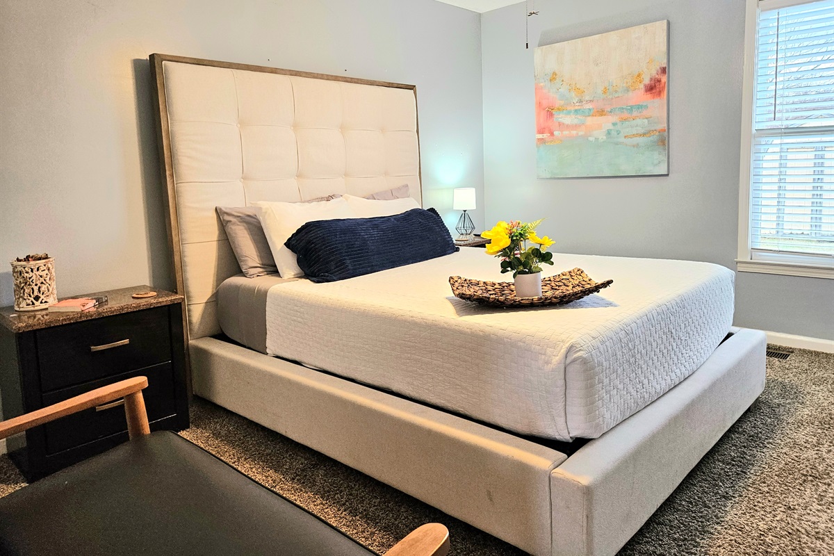 Queen primary bedroom with extra seating, ceiling fan, fast WIFI, TV, ensuite bathroom, and walk-in closet. Big window overlooking the fenced back yard adds fresh natural light and appeal.