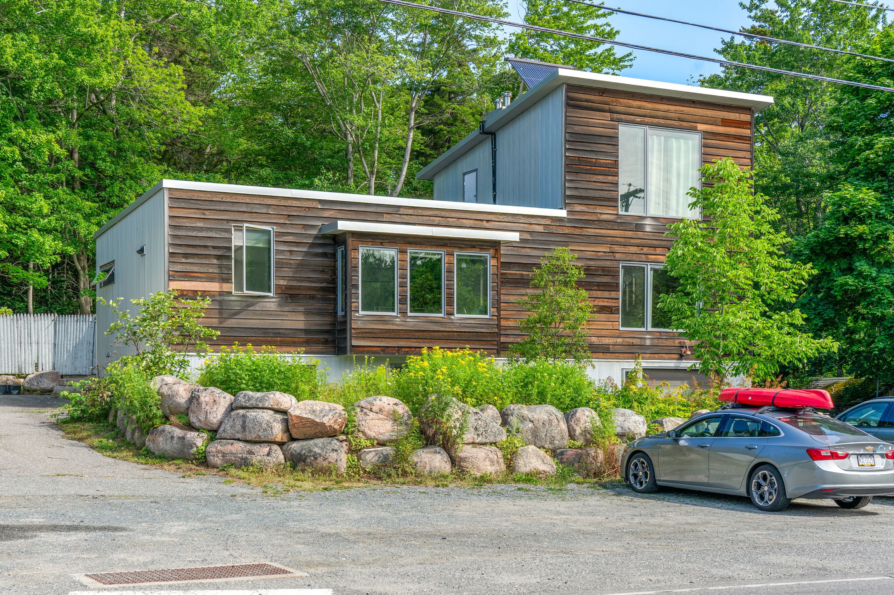 Bold architectural exterior of The Crag in the heart of Otter Creek village. Located just steps from the iconic Acadia Hot Showers and local general store, this modern retreat serves as your private backdoor entrance to Acadia National Park.