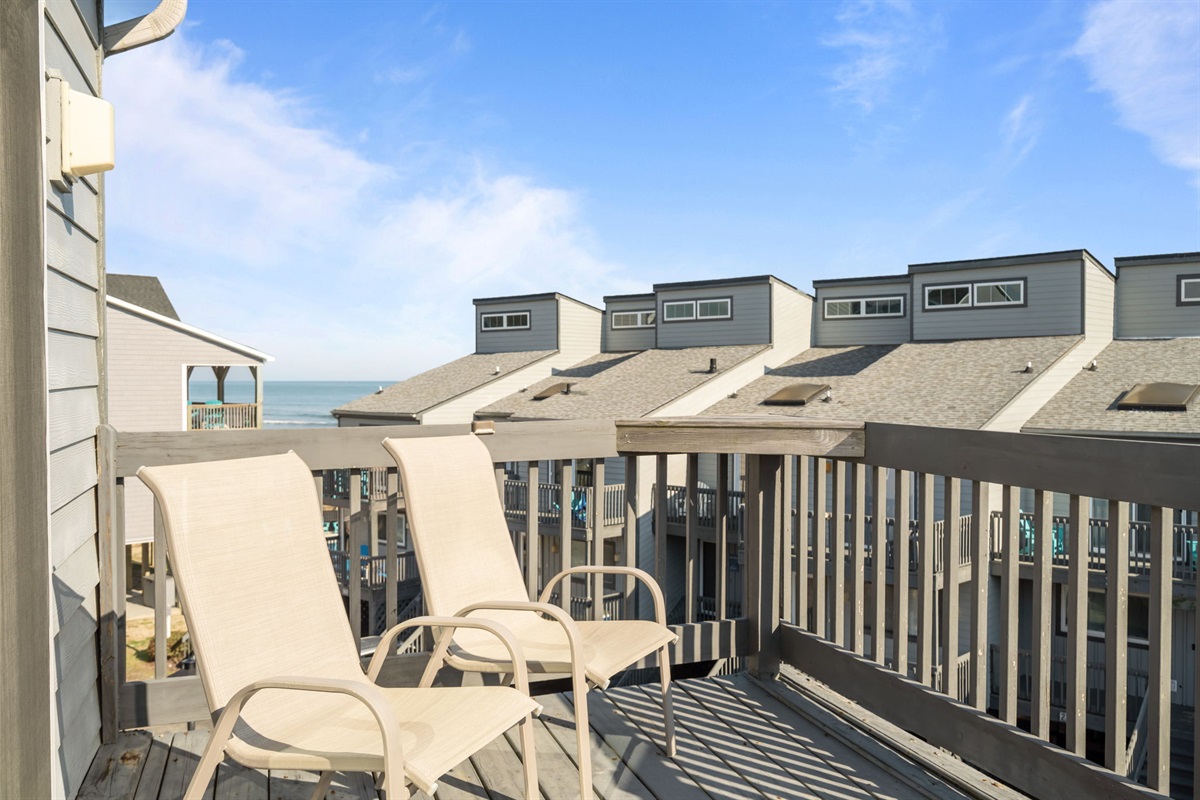 Upper level deck with chairs and partial ocean views between the neighboring beach homes