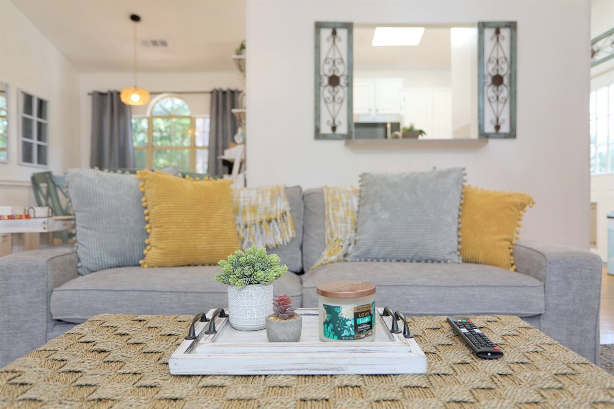 Relax in the bright and spacious living room with high ceilings, abundant natural light from large windows, cozy seating, and a smart TV for your entertainment.