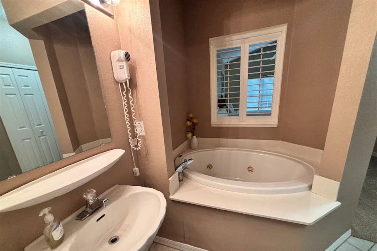 Bathroom with a soaking tub, pedestal sink, and bright natural light from the window.