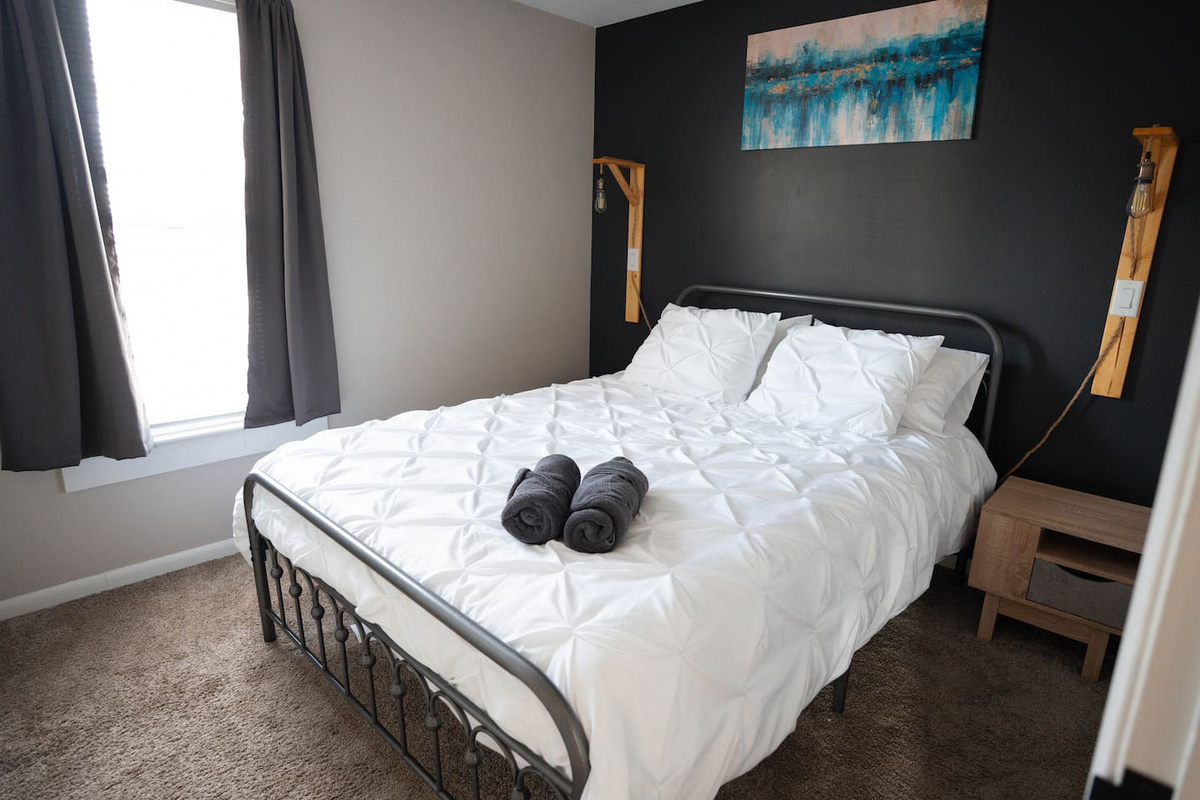 The bedroom has a comfy queen bed with fresh linens and plenty of pillows. Two nightstands with lamps make it easy to read or relax before bed. Curtains keep the space private and cozy, so you can get a good night’s rest.