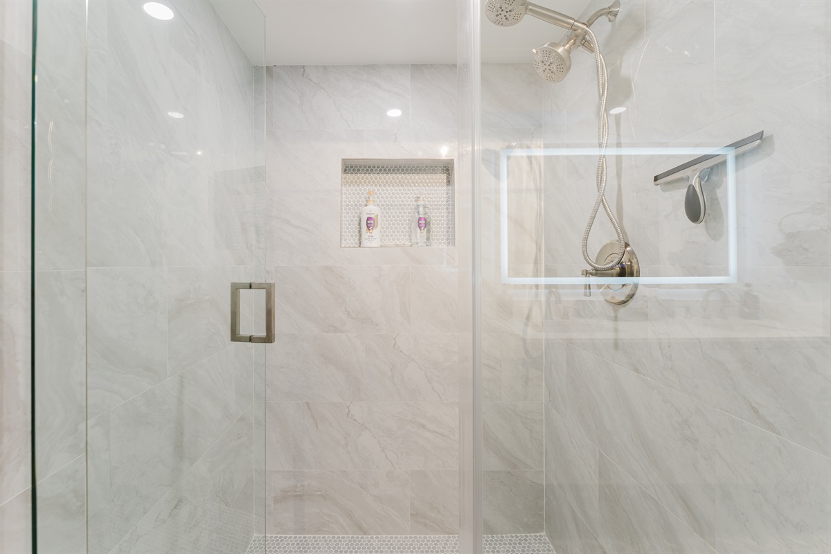 Spacious primary bathroom with double vanity, LED-lit mirror, and modern walk-in glass shower
