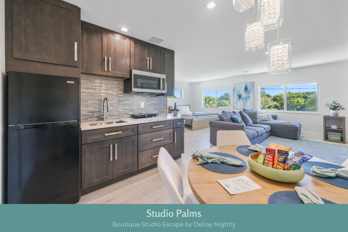 Bright, open Studio Palms pairs a modern kitchenette, dining space and comfortable lounge with large windows and a dedicated sleeping area—an inviting Delray Beach studio for couples, solo travelers or extended stays near downtown.