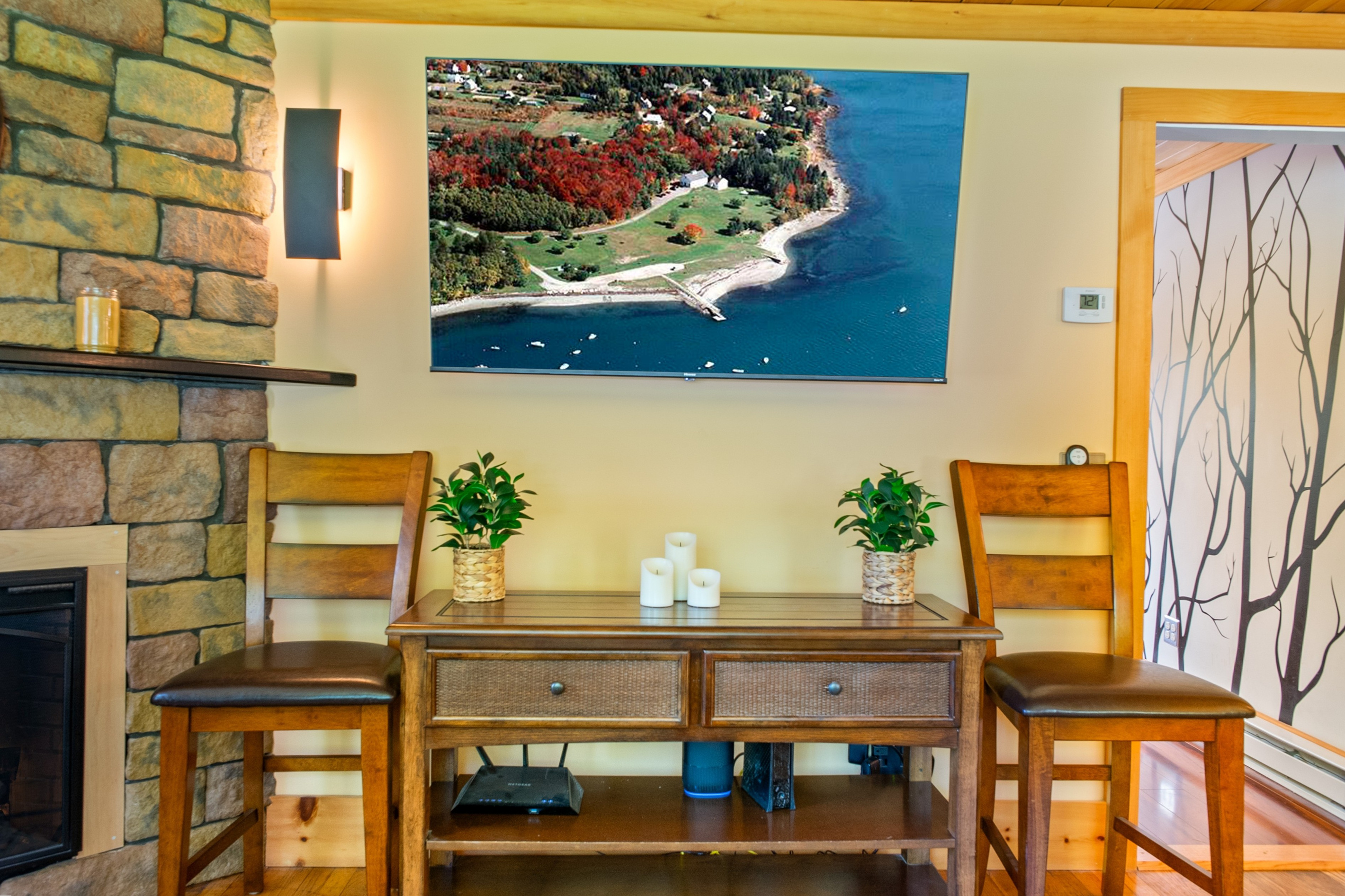 Stream your favorite shows on the large wall-mounted smart TV positioned directly above a wooden media console table. Flanked by extra dining-height chairs, this station is situated right next to the stone fireplace facade in the living room.