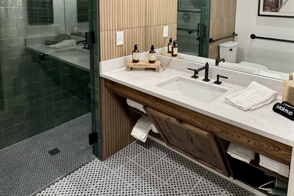 Homestead Suite ADA bathroom &mdash; accessible vanity, ADA-height fixtures, and designer sconce lighting in modern Western finishes at Gaines Ranch on the Square.
