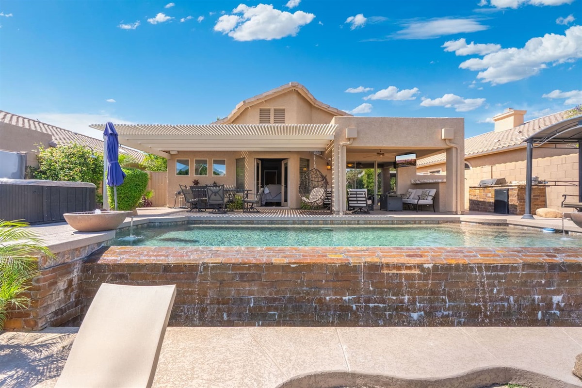 The pool's cascading waterfall feature adds a soothing soundtrack to your outdoor experience — cool off with a swim, then dry off on the sun deck with views of the covered patio beyond.