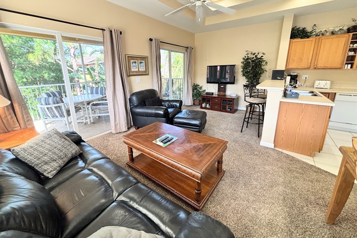 Comfortable living area with high ceilings, tile flooring, cozy seating, and two sets of sliding glass doors that bring in natural light and lead out to the private screened balcony.
