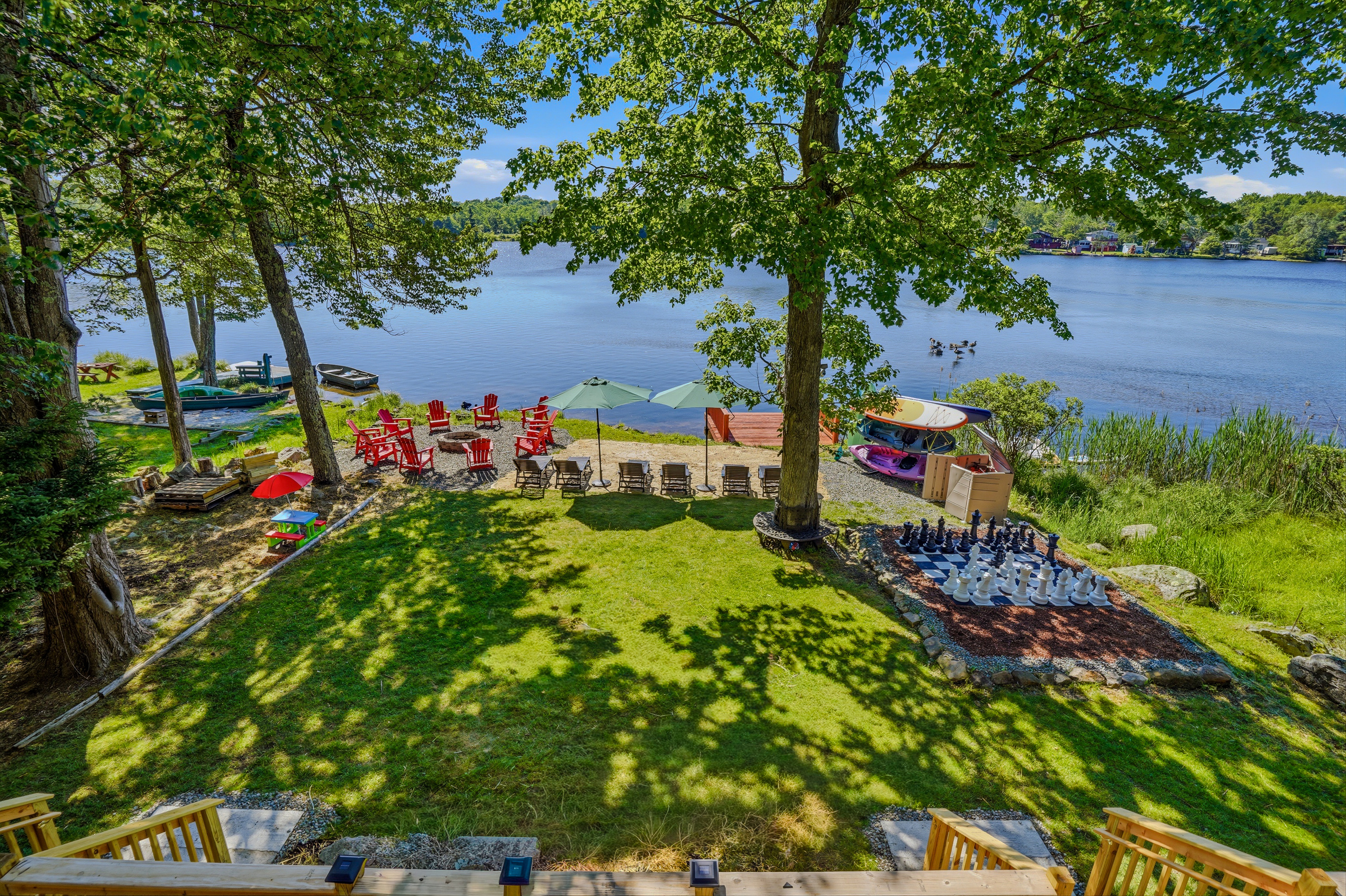 Backyard lawn view toward Lake Carobeth — dock, fire pit area, and red chairs in the distance