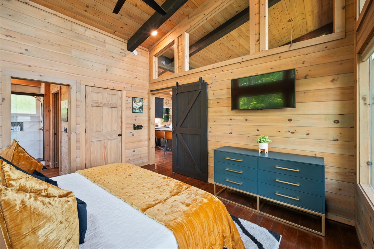 This cozy bedroom features rustic charm with modern touches. Wood-planked walls, black beams, and a sliding barn door that adds character and privacy.