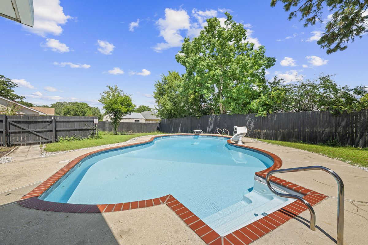 A freeform brick-trimmed pool surrounded by mature trees and a fully fenced yard for total privacy.