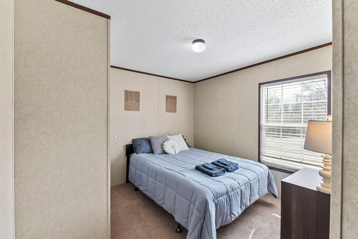 Cozy bedroom with a comfortable queen bed, soft natural light, and a large window creating a bright and relaxing space.