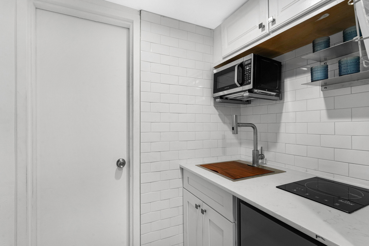The compact kitchen has a two-burner electric cooktop, microwave and deep sink, fully stocked with cookware and dishes for everyday cooking.