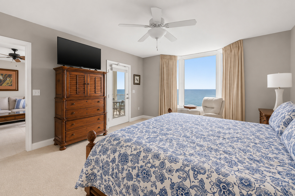 Master bedroom contains a dresser, smart TV, en suite bathroom, bay window, and door leading to balcony