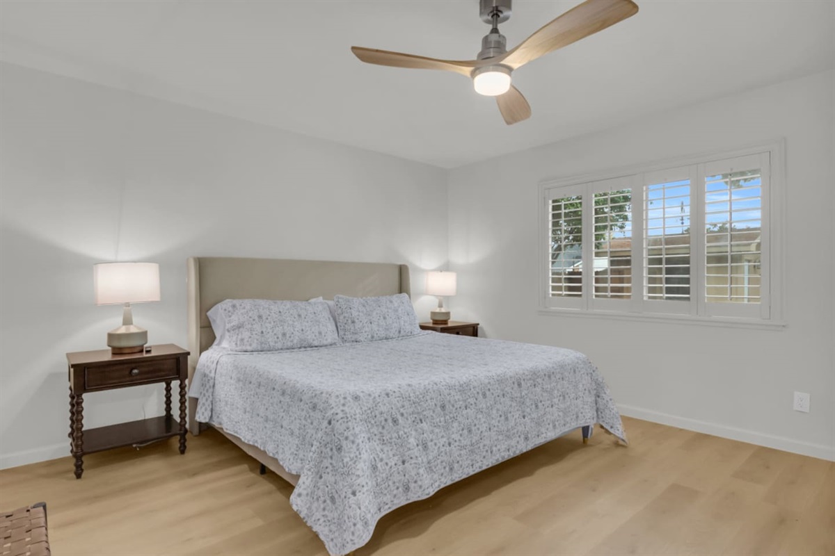 Spacious primary suite with a plush king bed, room darkening shades, crisp bed linens, and a quiet ceiling fan. A perfect retreat with soft natural lighting.