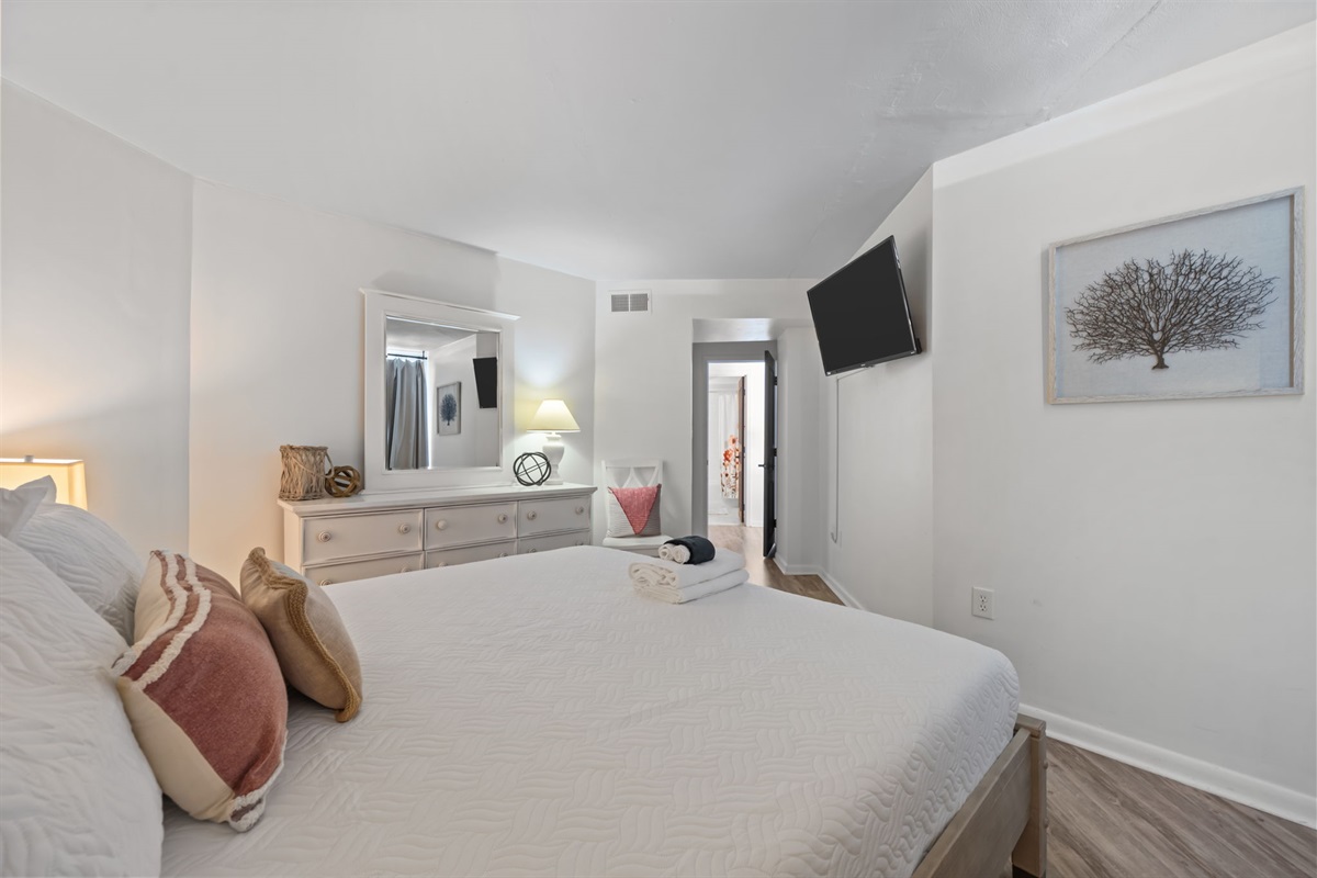 Comfort-forward 2nd bedroom with soft neutrals, a spacious dresser, and TV for laid-back evenings