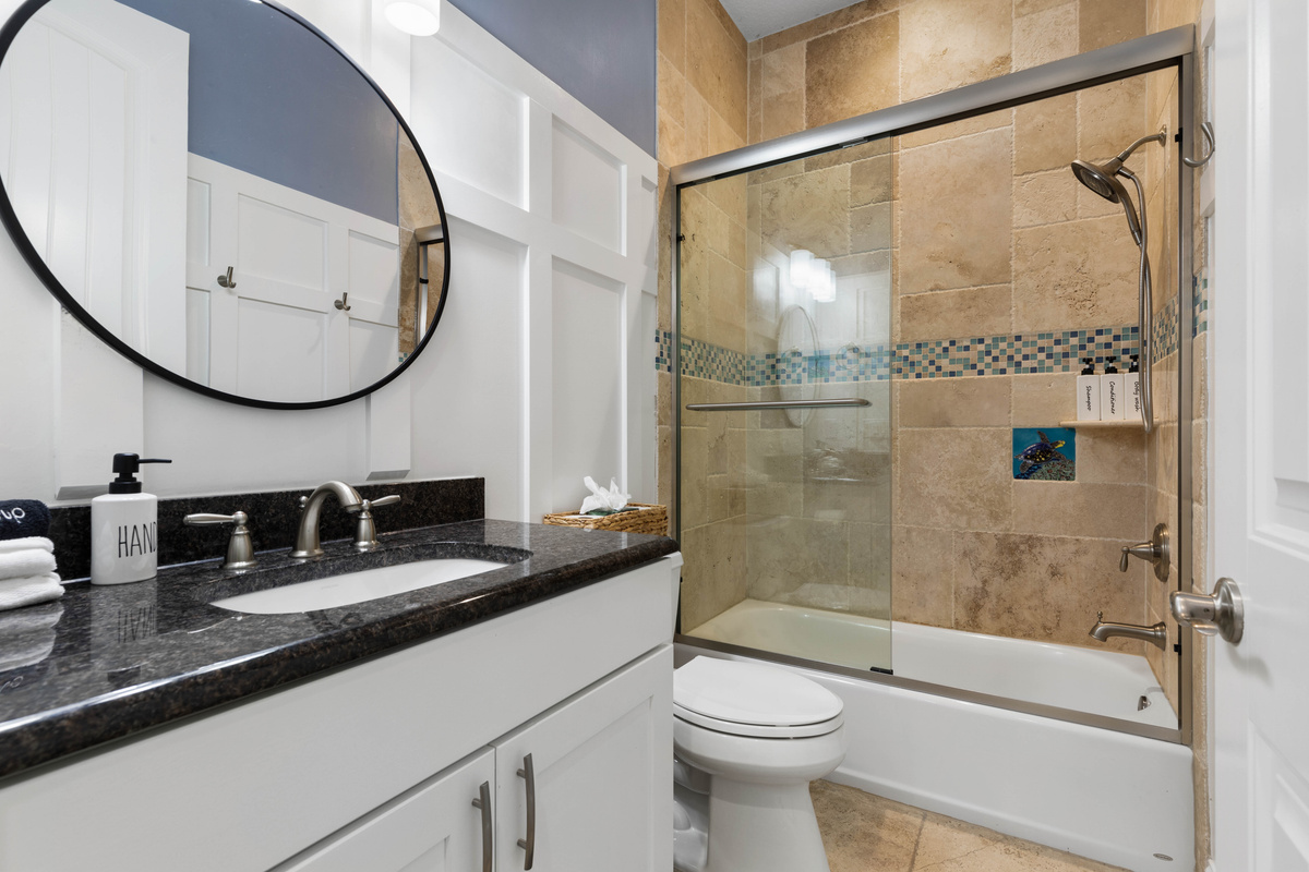Periwinkle bath with sliding glass tub doors, a handheld shower and a sea turtle tile that kids will want to spot.