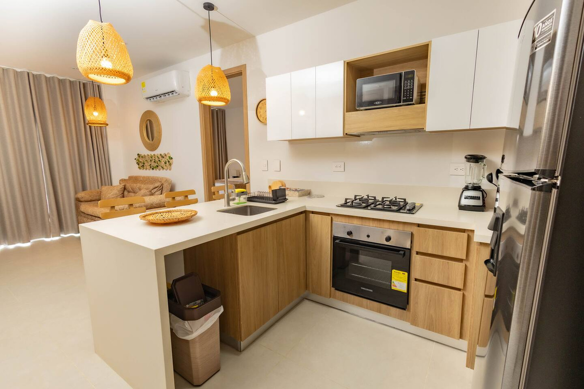 Los gabinetes de madera cálida, las lámparas colgantes de fibras tejidas y las encimeras claras crean un ambiente tranquilo de apartamento tipo resort, desde la cocina hasta la sala de estar.