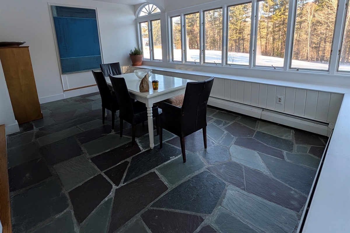 Sun-filled dining area with slate floors and expansive windows offering peaceful woodland views.