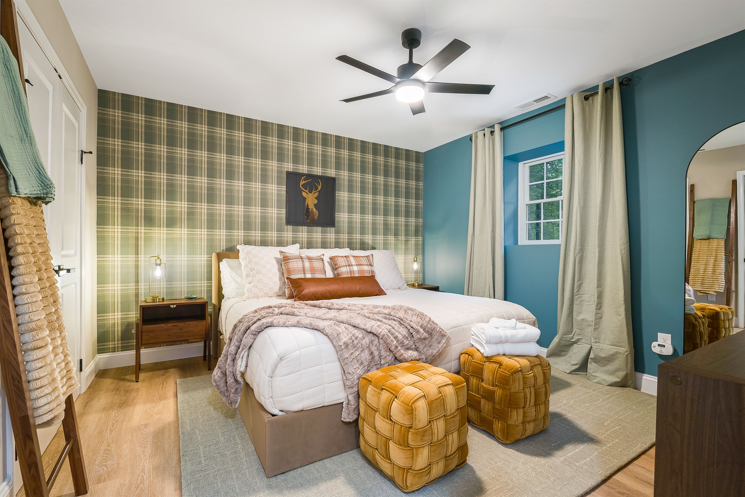 This bedroom pairs modern comfort with classic lodge charm, featuring a king bed against a plaid accent wall, earthy green tones, and warm textures. A cozy retreat with style and personality.