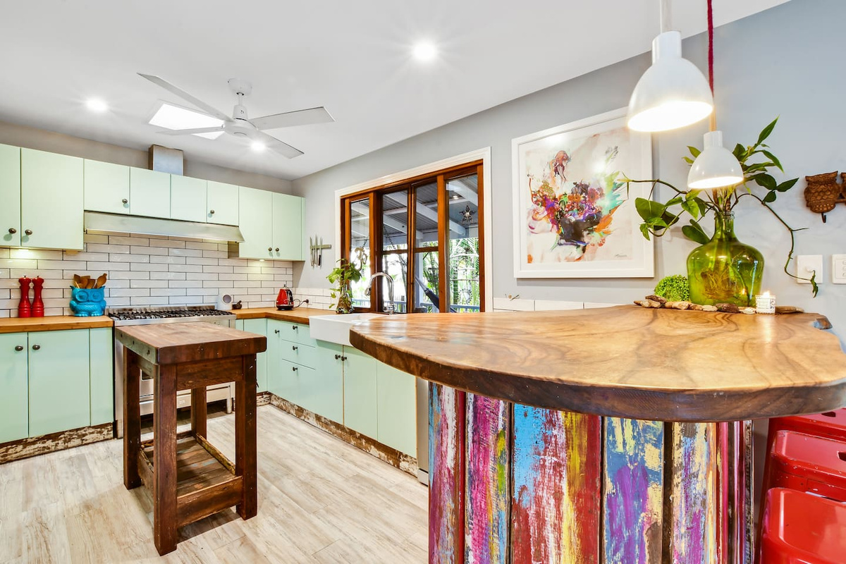Timber-framed windows bring garden greenery into the kitchen at Aaron's Beachside Boat House, giving the space a bright connection to the tropical surroundings.