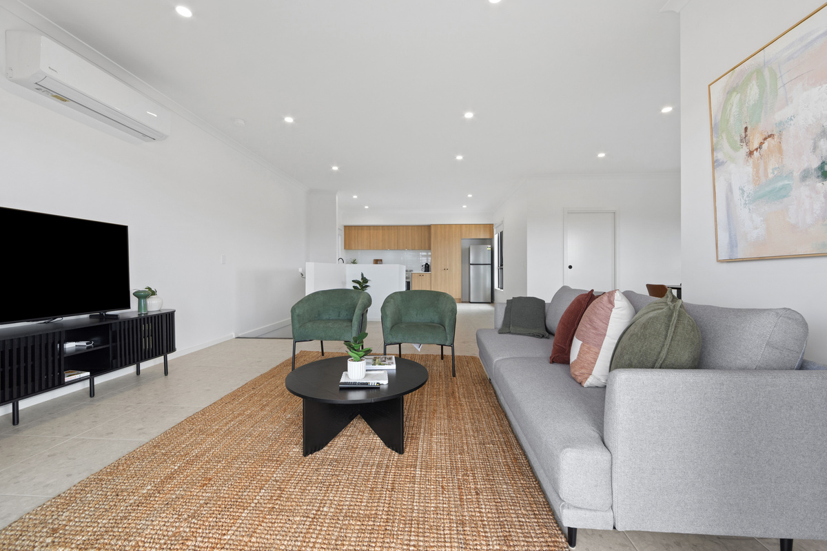 Upstairs lounge with a large smart TV on a media unit, grey sofa, armchairs and coffee table, with split-system air conditioning above.