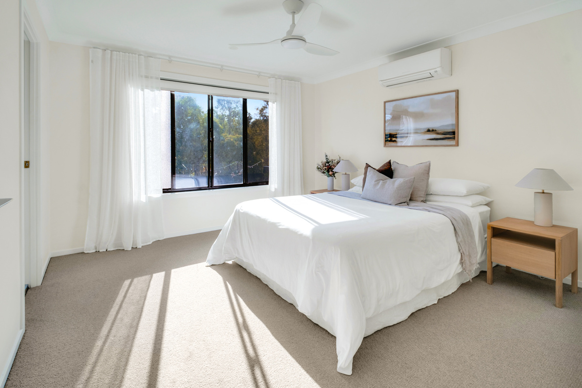A peaceful bedroom retreat with a comfortable bed, plenty of natural light, air conditioning and a ceiling fan.