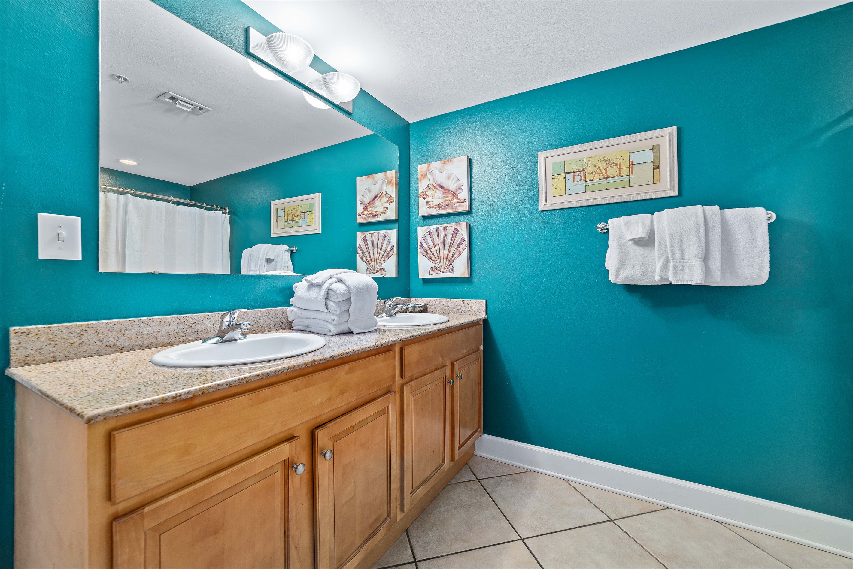 Start and end your day in this bright, functional primary bathroom. It includes a double vanity, a large mirror, and a shower/tub combo, all styled with a fun, beach-themed flair.
