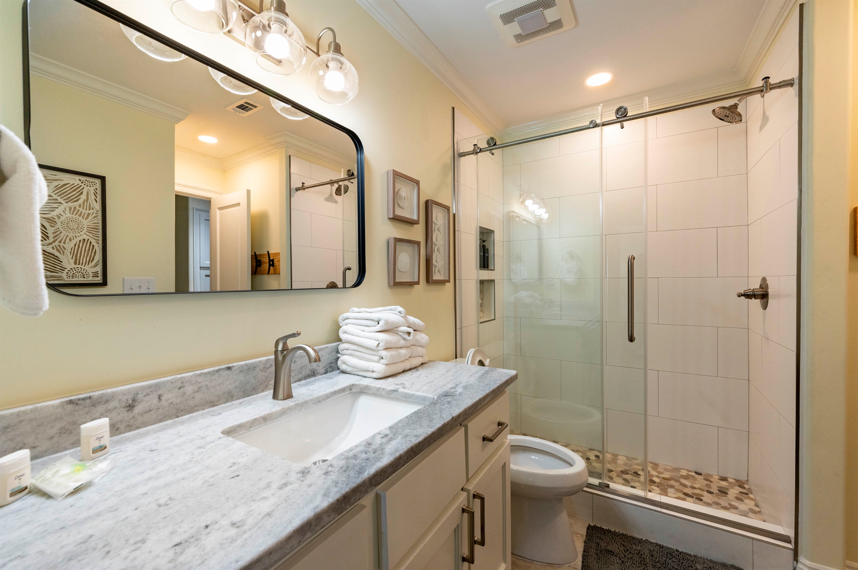 Modern beach-inspired bathroom with sleek shower, marble countertop, and fresh towels.